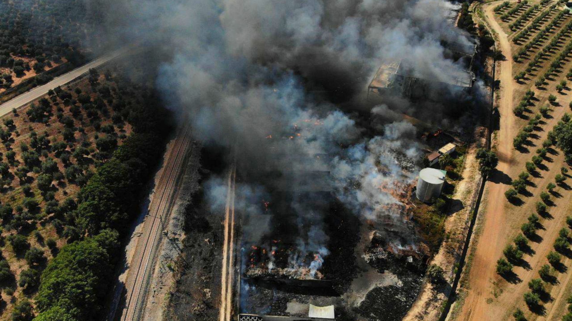 Incendio en planta de reciclaje de residuos vista aérea con columna de humo negro extendiéndose sobre zona agrícola en España
