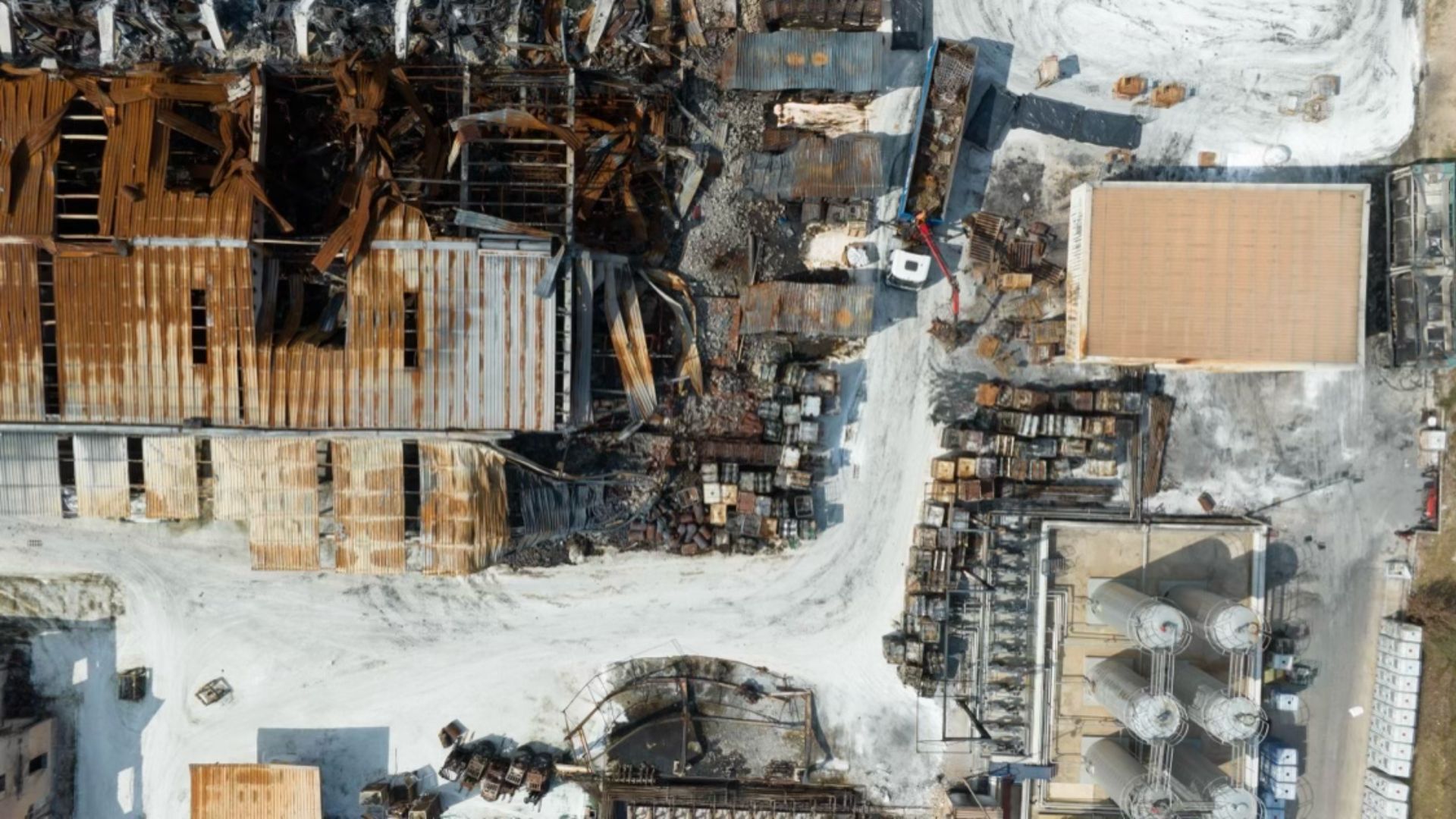 Vista aérea de una planta química devastada por un incendio industrial con estructuras colapsadas y depósitos de almacenamiento afectados