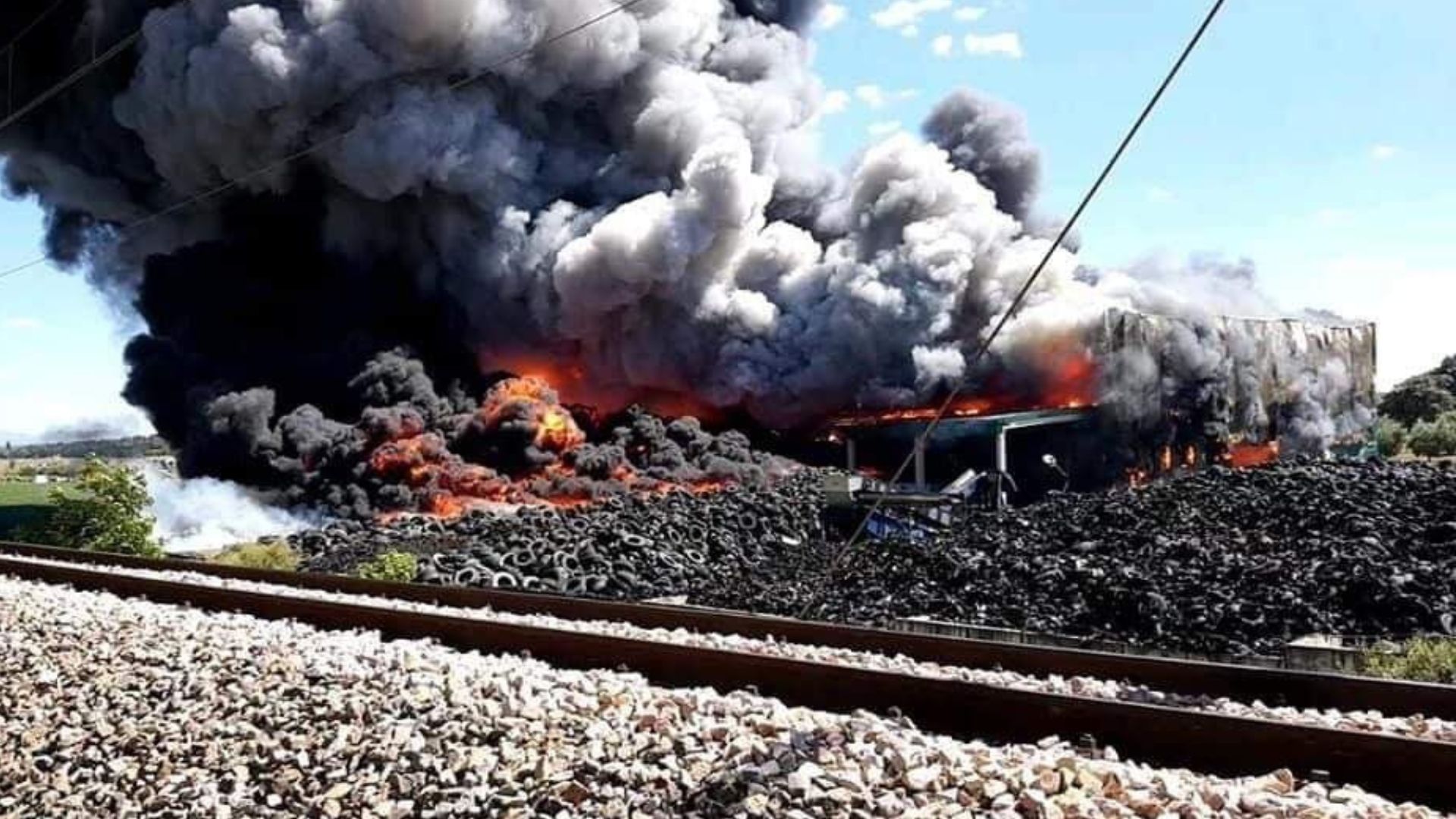 Incendio en planta de reciclaje de neumáticos con combustión de plásticos generando nube de humo tóxico sobre instalación industrial